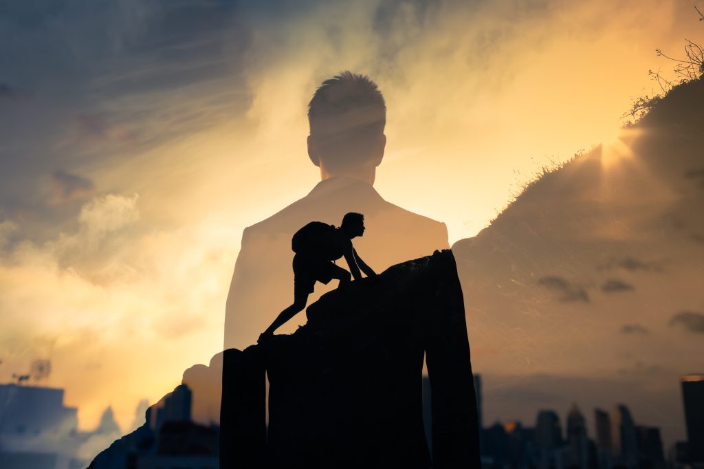Man feeling determined climbing up a steep mountain side.