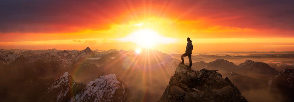 Adventure Composite of Man Hiking on top of a rocky mountain peak. Background Landscape from British Columbia, Canada. Sunrise Dramatic Colorful Sky